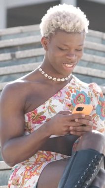 Dışarıdaki merdivenlerde cep telefonu kullanan şık bir Afrikalı transseksüel. Teknoloji ve sosyal medya kavramı. Dikey görüntüler
