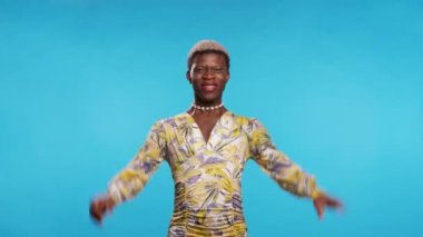 Heyecanlı Afro-Amerikan model şık elbiseler içinde yumruklarını sıkıyor ve mavi arka plana karşı zafer kazandıktan sonra gözleri kapalı bağırıyor.