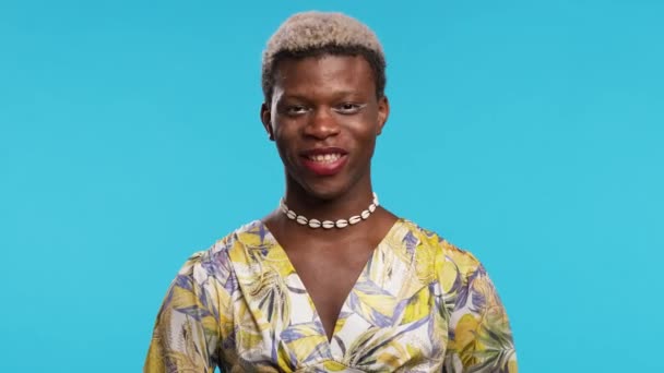 穿着粉色衣服和项链的快乐自信的非洲女性模特站在蓝色的墙边 双手插在腰部 看着镜头 — 图库视频影像