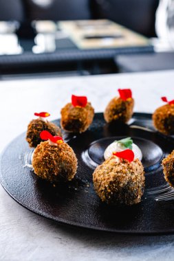 Beyaz masaya konmuş siyah tabakta servis edilen çiçek yapraklarıyla süslenmiş iştah açıcı kroketler. Tipik İspanyol yemeği.