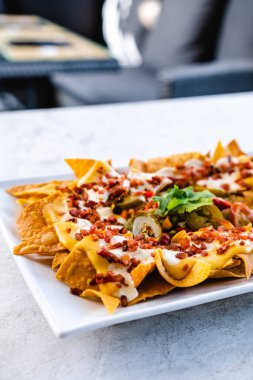 Beyaz seramik tabakta çeşitli soslar ve jalapenolarla servis edilen iştah açıcı nacholar.