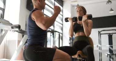 Spor salonunda yetişkin bir kadına ağırlık kaldırmayı öğreten bir erkek eğitmenin yavaş çekim videosu.