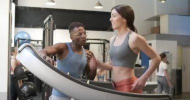 Heyecanlı bir eğitmenin spor salonundaki koşu bandında bir kadını motive edişinin videosu.