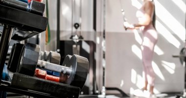 Çağdaş spor salonunda egzersiz yapan anonim bayan sporculara karşı raflara yerleştirilmiş birçok ağır halterler.