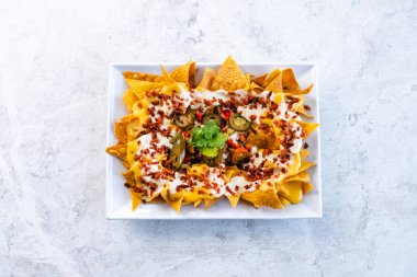 Beyaz seramik tabakta çeşitli soslar ve jalapenolarla servis edilen iştah açıcı nacholar.