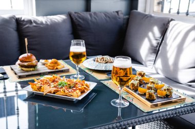 Hamburgerle nefis bir öğle yemeği ve kanepede bira bardaklarının yanında servis edilen nachos.
