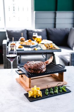 İştah açıcı balta bifteği tepside çeşitli atıştırmalıkların ve restoranda bir bardak kırmızı şarabın yanında servis ediliyor.