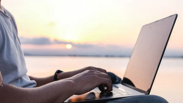 侧视图观察日落时在海上远程工作的匿名男性自由职业者在笔记本电脑上打字的情况 — 图库照片