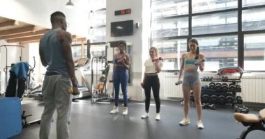 Modern spor salonundaki dambılları kullanarak beden eğitimi dersi veren bir eğitmenin yavaş çekim videosu.