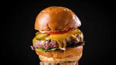 Lezzetli hamburgerin hamburgerini marullu ve peynirli domatesli ve turşulu siyah arka planda dönen turşulu kızartmayı durdurun.