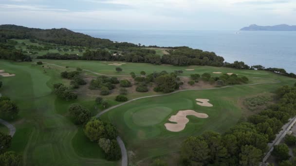 スペインのマヨルカの曇った空に向かって穏やかな青い海の上の丘の上の緑のゴルフコースと緑のゴルフコースの息をのむような空気の眺め — ストック動画