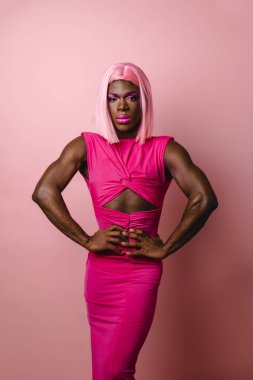 Pembe elbiseli ve peruklu kendinden emin Afrikalı transseksüel izole edilmiş pembe arka planda poz verirken kameraya bakıyor..