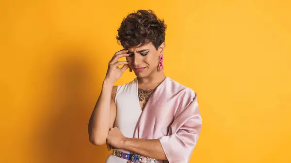 Üzgün ve endişeli bir adam kameraya bakıyor. Sarı arka planlı bir fotoğraf stüdyosunda duruyor.