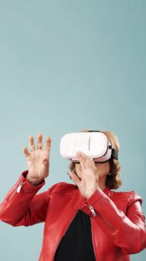 Üst düzey kadın, mavi arka planda dikilirken sanal gerçekliği VR gözlükleriyle yaşıyor. Teknoloji ve yenilik kavramı.