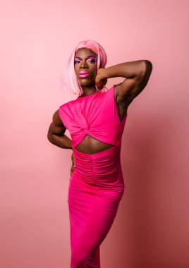 Dar pembe peruklu ve renkli makyajlı özgüvenli Afro-Amerikan travesti mankeni stüdyoda el pençe divan duruyor.