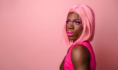 Genç kendinden emin Afro-Amerikan transseksüel model pembe peruk takıyor ve makyajla omuzlarına dokunuyor.