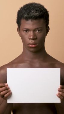 Ciddi bir Afrikalı transseksüelin atölyesindeki videoda mesaj göstermek için elinde boş bir poster var.