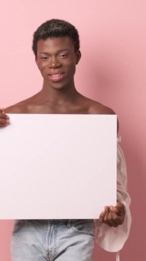 Afrikalı transseksüel, izole bir arka planda boş bir beyaz poster tutarken gülümsüyor. Reklam kavramı.