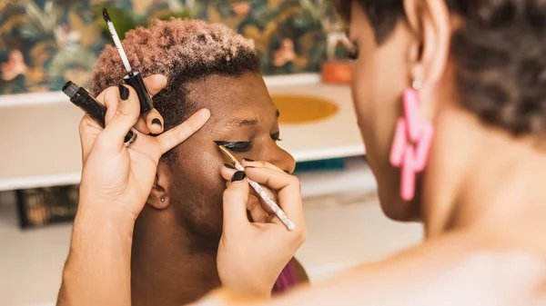 Close up of a black transgender man with his eyes closed as a colleague applies make-up in a dressing room