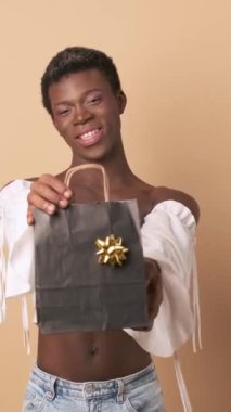 Afrikalı bir transseksüel, elinde tutarken gülümsüyor ve izole bir arka plan üzerinden birine hediye veriyor..