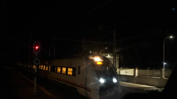 照らされた鉄道駅に入る商品列車のリアルタイムビューとプラットフォーム上の立っている列車と暗い夜の時間に赤信号を交差 — ストック動画