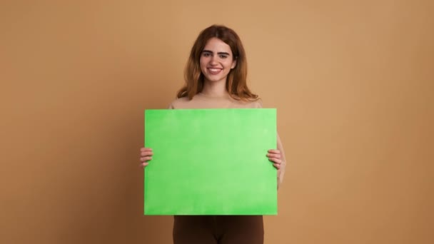 有米色背景的工作室视频 一个年轻女人拿着一个绿色的面板笑着和难过的样子 — 图库视频影像