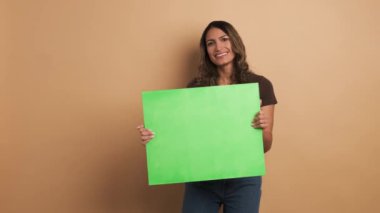 Elinde yeşil bir pankart tutan ve baş parmağını kaldıran gülümseyen bir kadının bej arkaplanlı videosu.