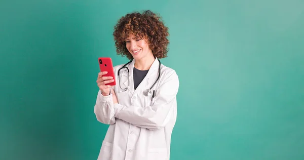 Female doctor looking at screen of mobile phone while standing browsing and showing thumb up gesture on finding music tune