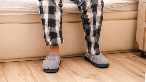 Legs of an adult man putting on slippers when getting out of bed in pyjamas