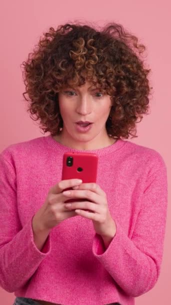 Excited Young Woman Pink Casual Clothes Curly Hair Checking Smartphone — Stock Video