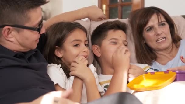 自宅で一緒にキャンディーを食べながらテレビを見ている非規範的な家族のビデオ — ストック動画
