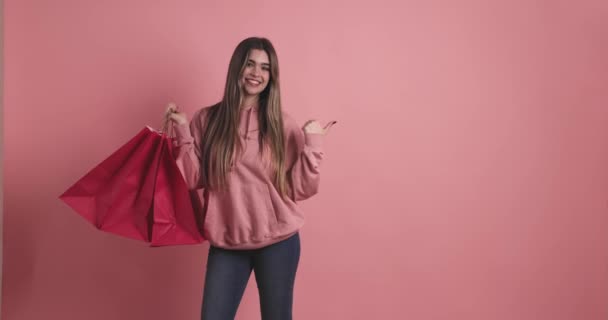 Junge Frau Hält Einkaufstaschen Zur Seite Atelier Mit Rosa Hintergrund — Stockvideo
