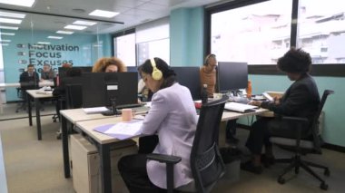 Yaratıcı çalışma alanlarında kendi masalarında otururken bilgisayar üzerinde çalışan çok ırklı iş arkadaşları