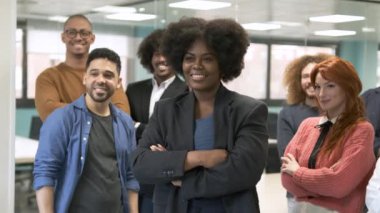 Yaratıcı ofiste grup fotoğrafı için poz verirken kolları çapraz duran Afro-Amerikan bayan yönetici.