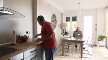 Yetişkin bir adamın mutfağı temizlerken gay bir çiftin ve torununun masada oturup oyun oynamalarının videosu.
