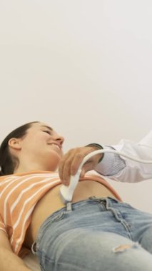 Modern klinikte kanepede yatan kadın hastaya ultrason yapan mutlu, olgun bir erkek doktorun yavaş hareketi.