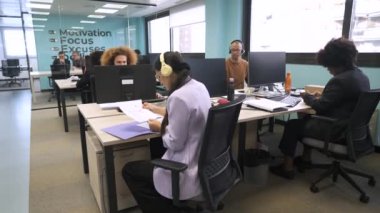 Bilgisayarlı masalarda oturan ve modern çalışma alanında çalışan çok ırklı iş arkadaşlarının yavaş çekimini kaldır