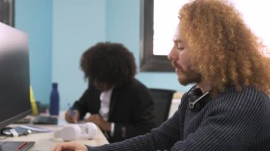 Masasında bilgisayar kullanan ve çalışma alanındaki kameralara bakan afro saç stili olan mutlu genç yaratıcı iş adamı.