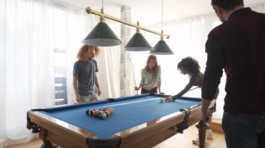 Genç siyahi bir kadının, aydınlık odada çok ırklı arkadaşlarıyla bilardo oynarken ıstakayla topa vurması ağır çekim.