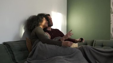Mutlu genç çift kanepede oturup film izlerken patlamış mısır yiyor ve hafta sonu evlerinde ilginç filmleri tartışıyorlar.