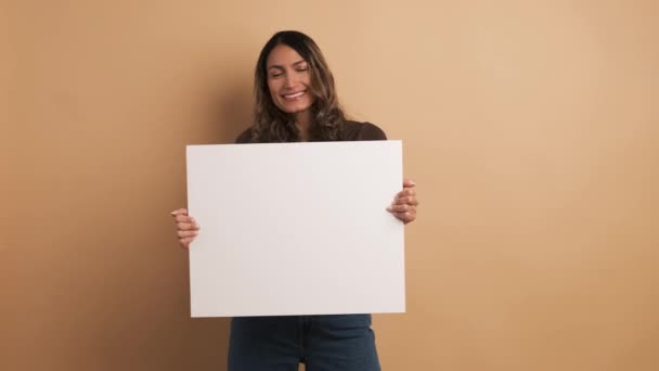 カメラで微笑んでいる間に白いパネルを保持している女性の茶色の背景を持つビデオ — ストック動画