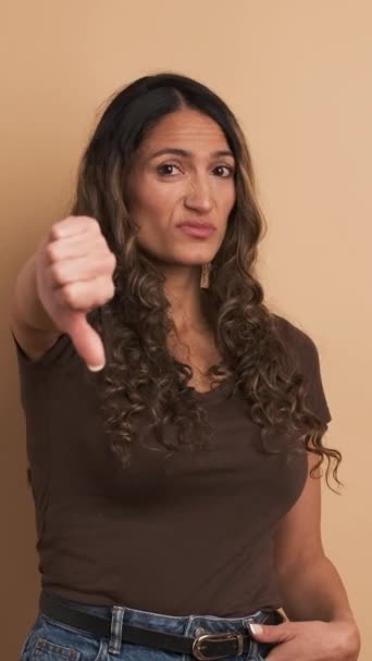 ヒスパニック系女性が親指の下で意見の相違を引き起こす茶色の背景を持つビデオ フッテージ — ストック動画