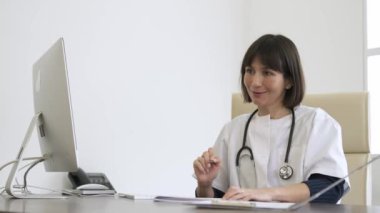 Klinikteki bilgisayar masasında danışmanlık yaparken reçete yazan ve konuşan mutlu genç bayan doktor.