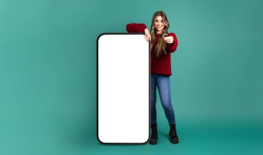 Gülümseyen genç bayan kameraya bakarken akıllı telefon şeklindeki reklam panosunun yanında duruyor ve yeşil arka plana karşı diş bandı sunuyor.