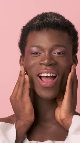 性格开朗的非洲裔美国变性者 光着肩膀 面容柔和地触摸着脸 微笑着 用粉红的背景看着相机 垂直镜头 — 图库视频影像