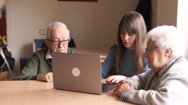 Genç bir bayanın masada oturup, yaşlılara evde netbook kullanmasını öğretmesi.