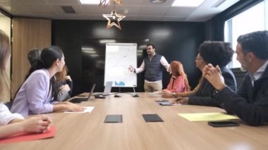 İş adamı, yaratıcı ofisteki konferans odasında beyaz tahtaya şemalar çizerek çok ırklı meslektaşlarına stratejiyi açıklıyor.