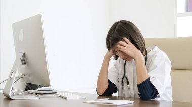 Stresli genç bayan doktor, klinikte çalışırken baş ağrısı çekerken bilgisayar başında oturuyor.
