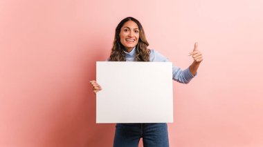 Elinde boş bir panel tutan ve etrafı gösteren bir kadının pembe arka planı.