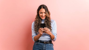 Gülümseyen bir İspanyol kadının pembe arka planı cep telefonu kullanıyor.
